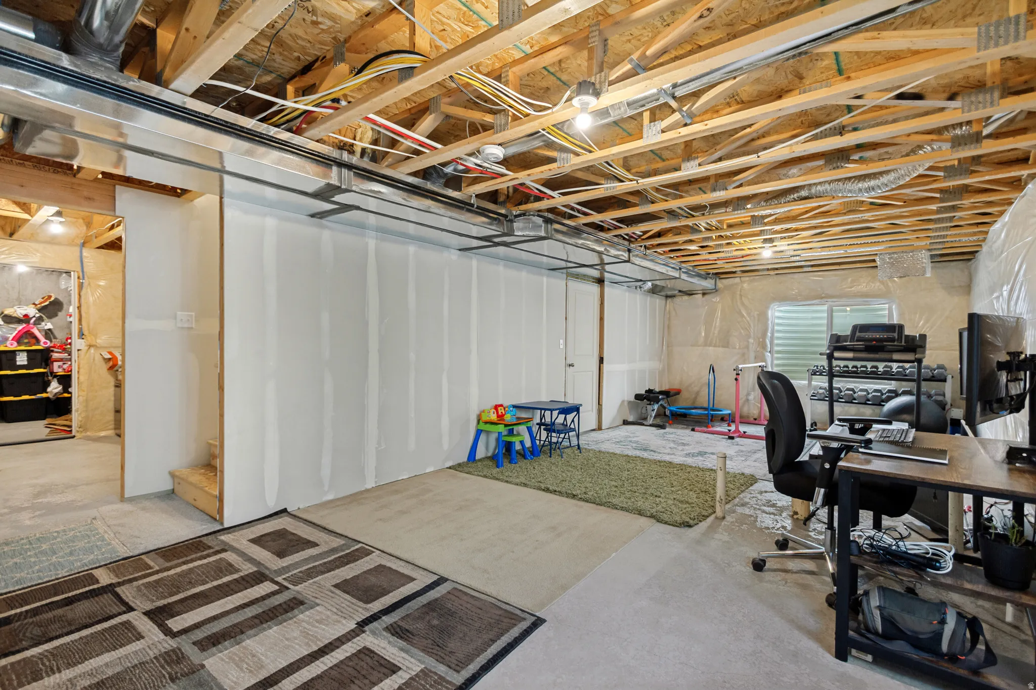 Unfinished basement featuring exposed wood joists, concrete flooring, and partial drywall installation