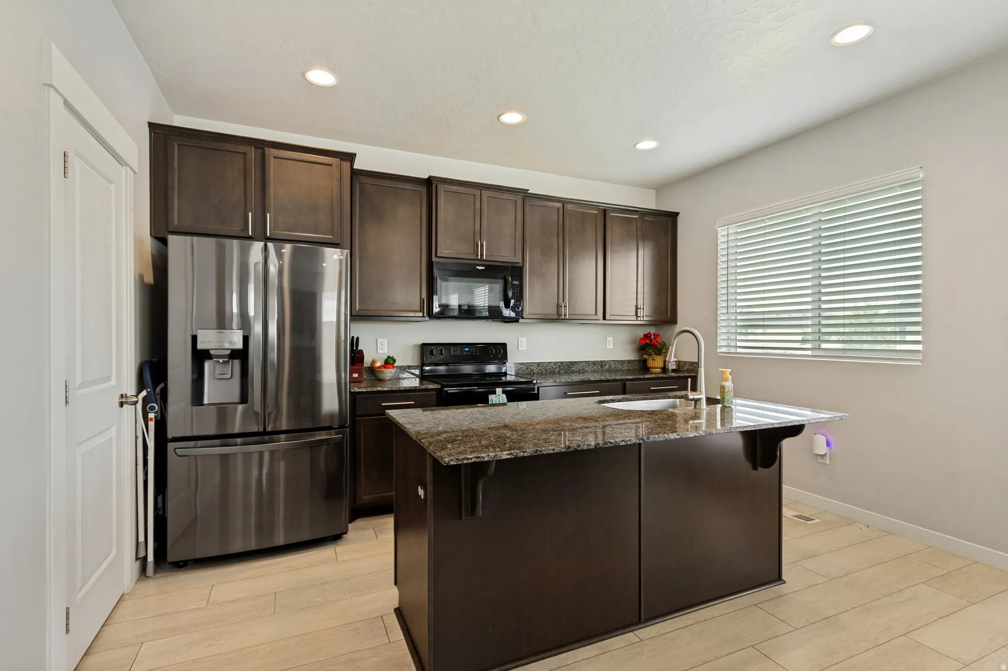 Kitchen featuring dark wood cabinetry, a center island with a stone countertop, recessed lighting, and stainless steel appliances