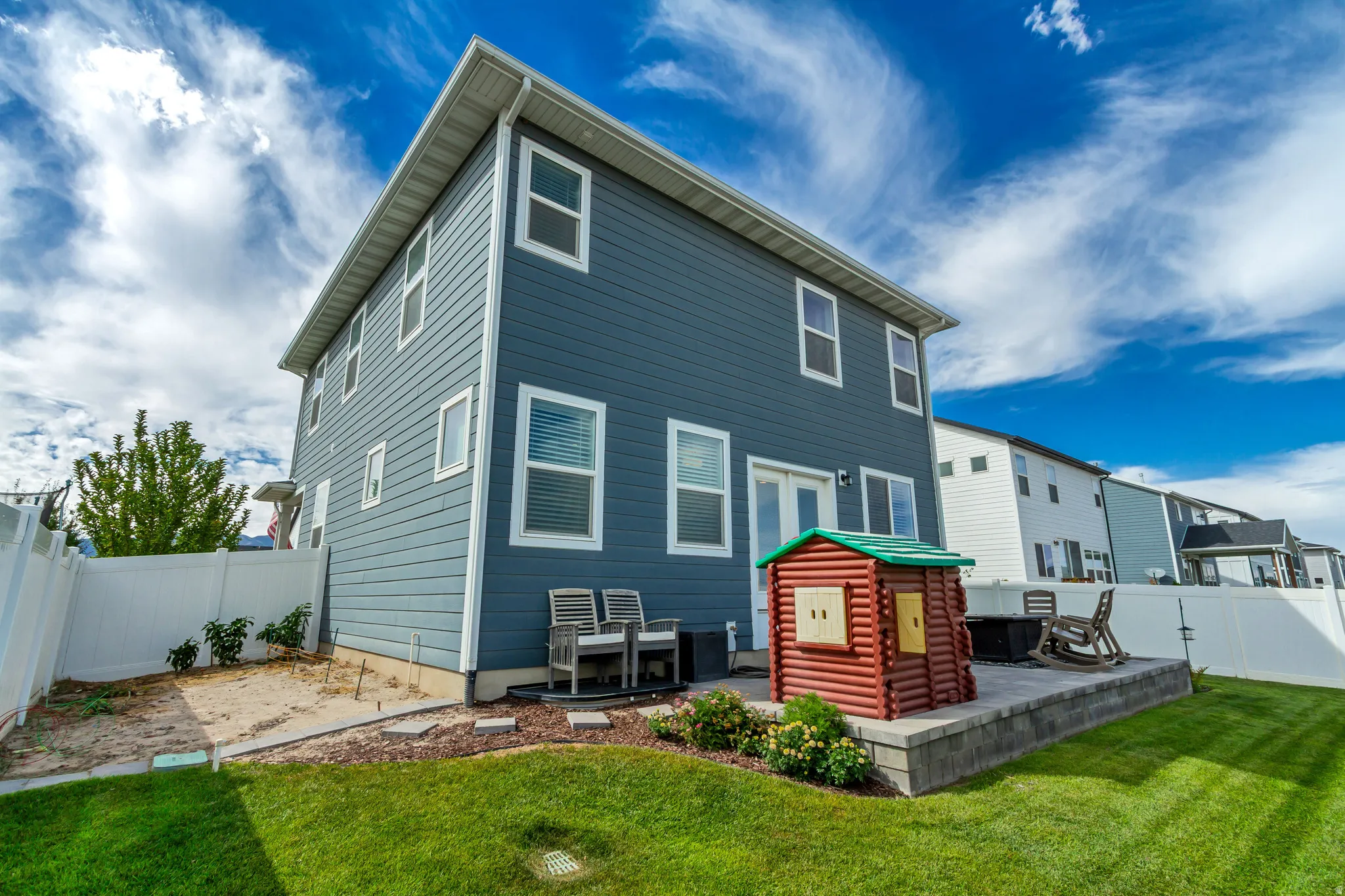 Blue siding exterior, white-framed windows, double glass doors, white privacy fencing, and a tiered patio with block retaining wall