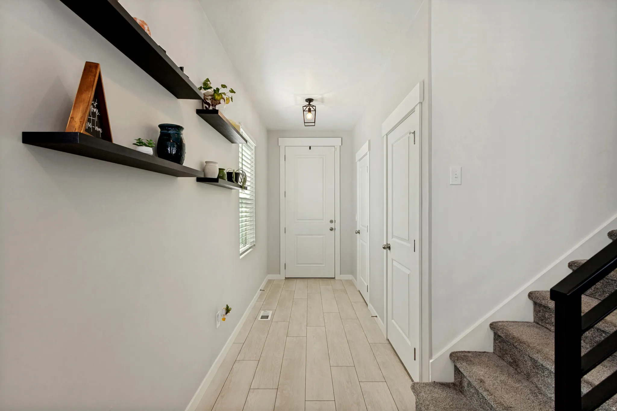 Light wood-finish flooring extending through the hallway, white doors with modern hardware, and a staircase with a black metal railing