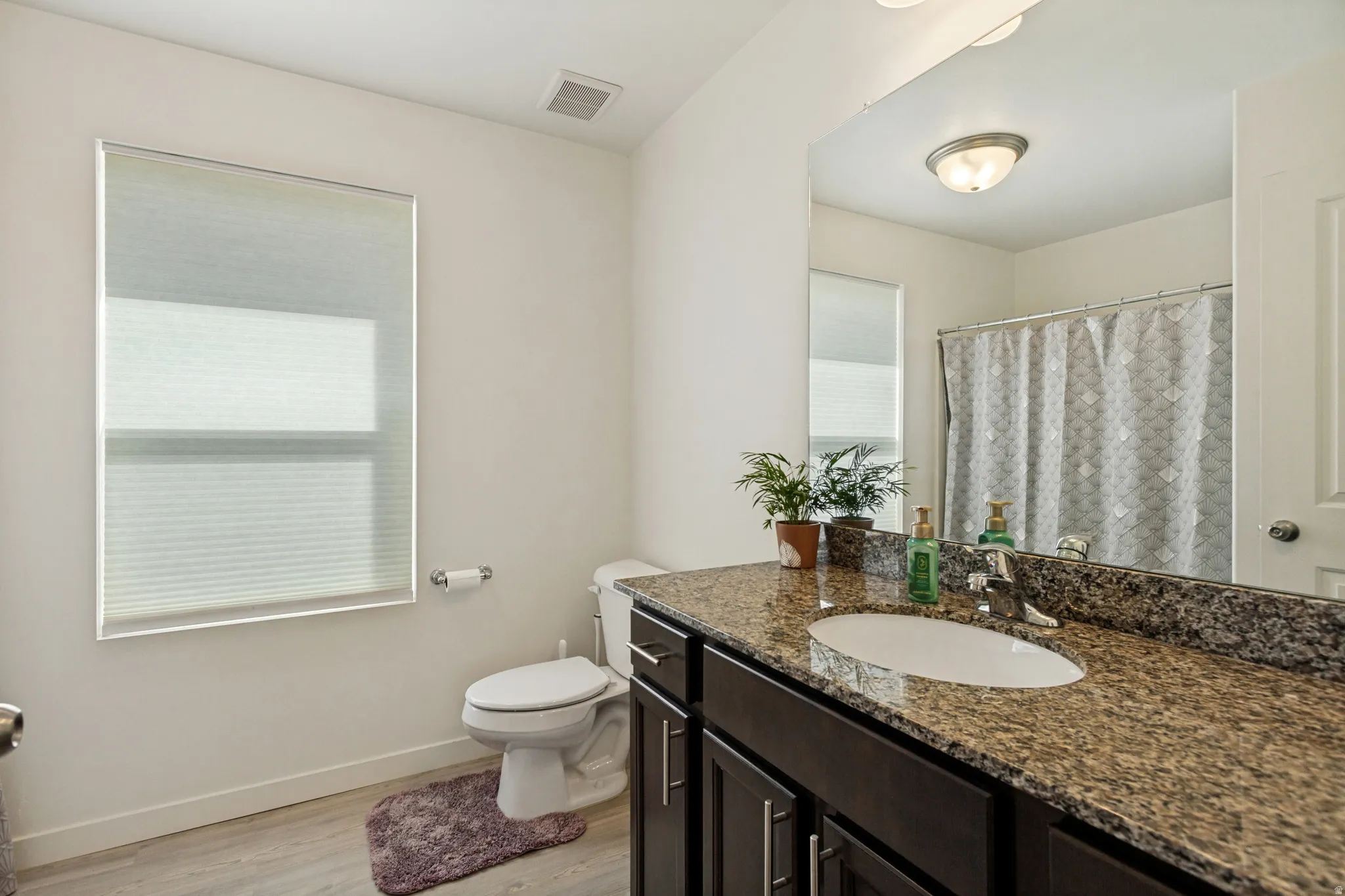 Bathroom featuring a single vanity with stone countertop, undermount sink, dark wood-finish cabinetry, and a full-width mirror