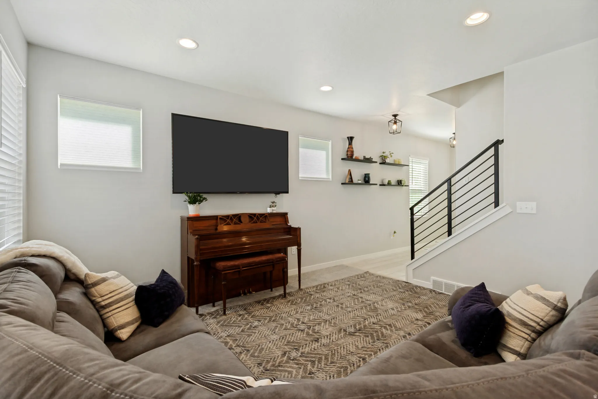 Recessed ceiling lighting, multiple windows with blinds, built-in shelving, and a modern stair railing