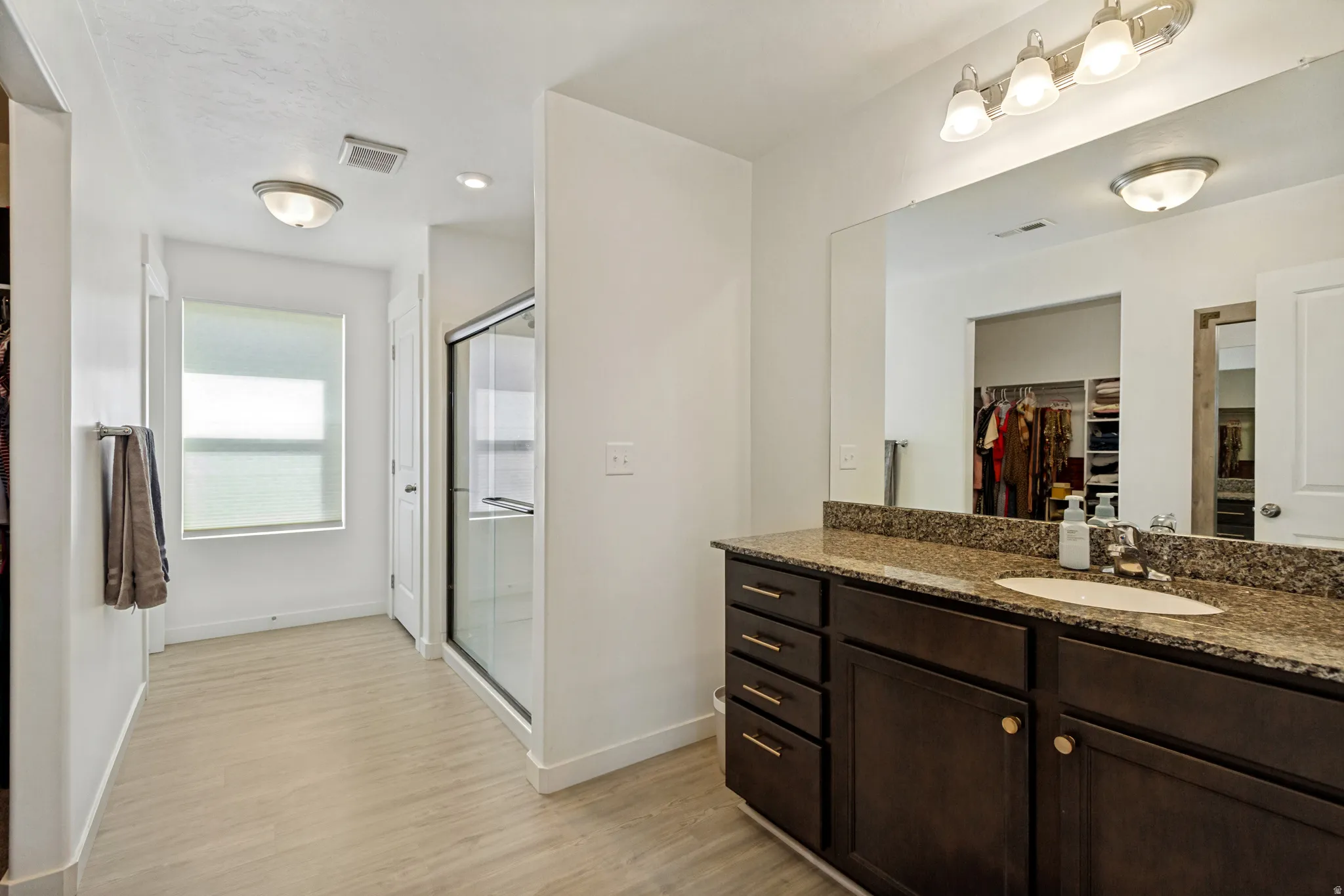 Wood-finish flooring throughout, vanity with a granite-style countertop, integrated sink, and dark wood cabinetry