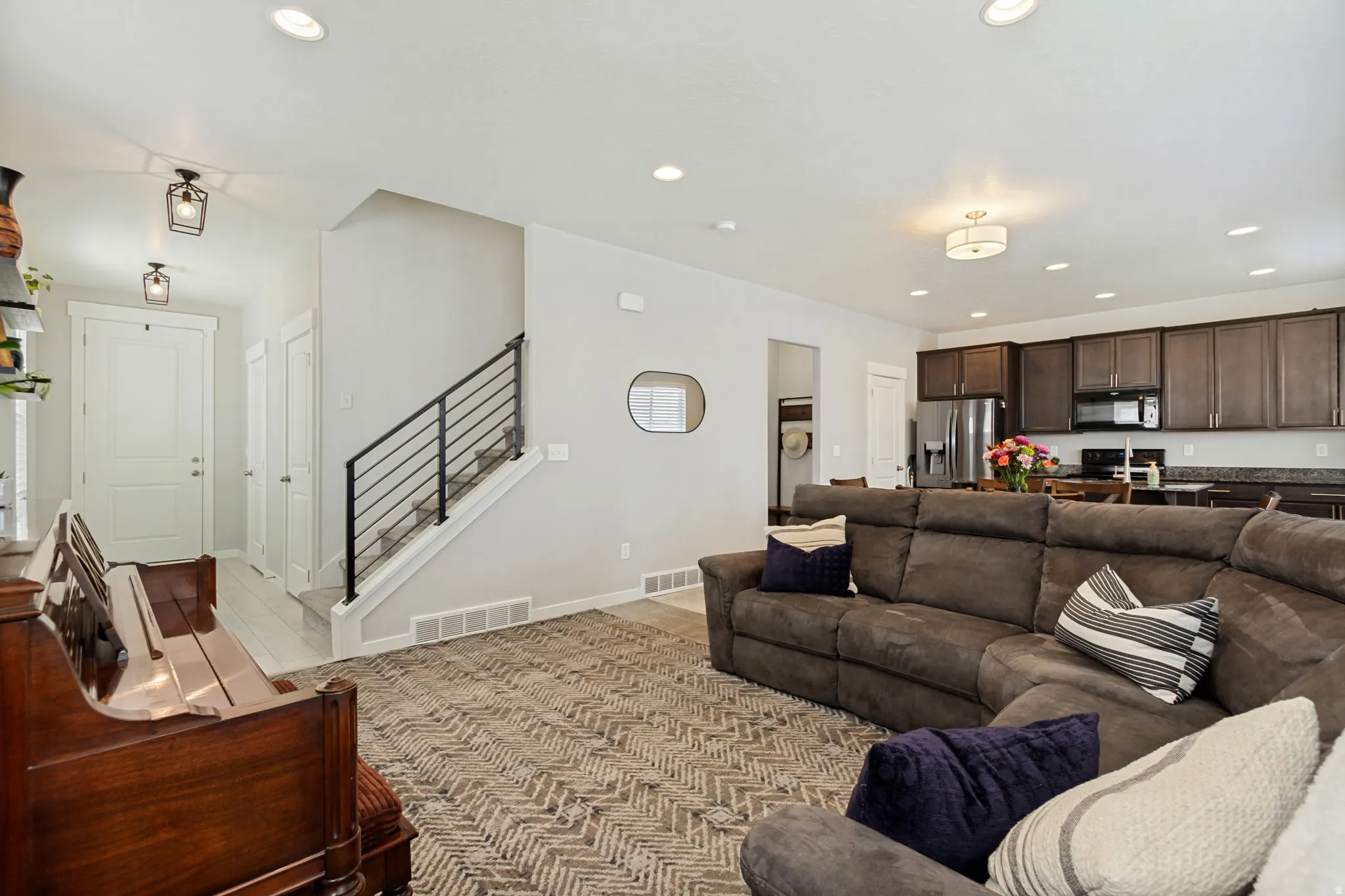 Open-concept living area with recessed lighting, a contemporary black metal stair railing, and wood-finish flooring