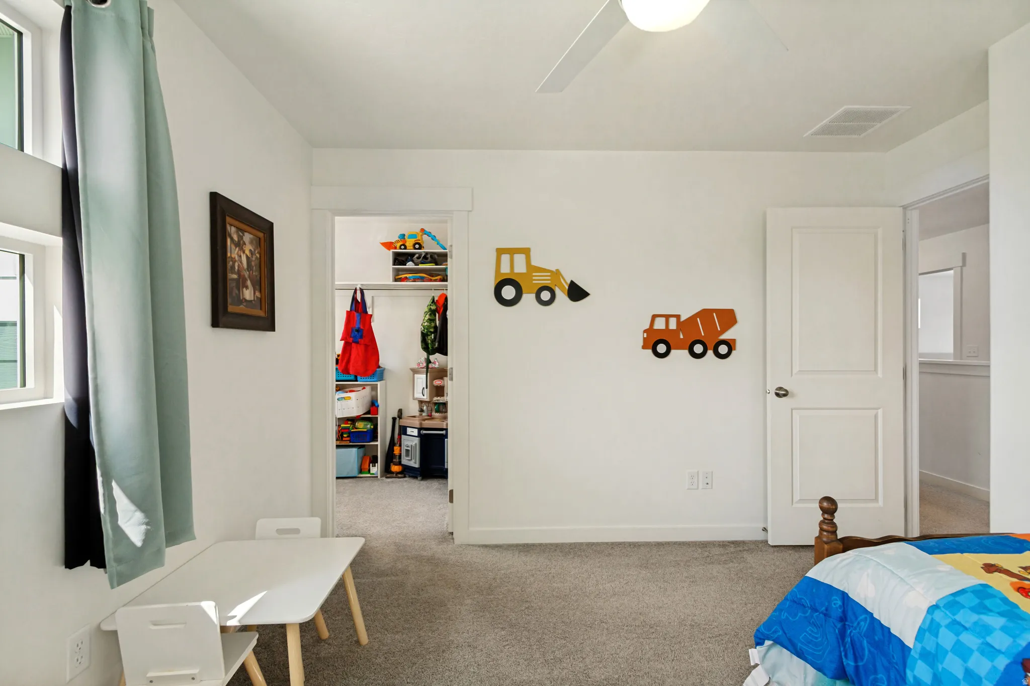 White painted walls with gray carpet flooring, an open doorway leading to a walk-in closet, and a ceiling fan with light fixture