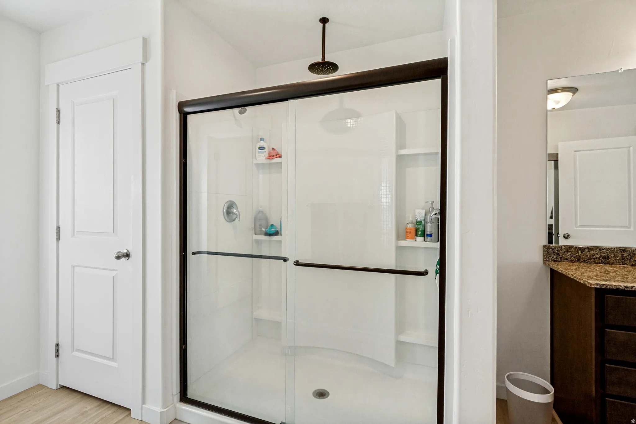 Walk-in shower with dark bronze framing and fixtures, built-in shelving, and a rain showerhead