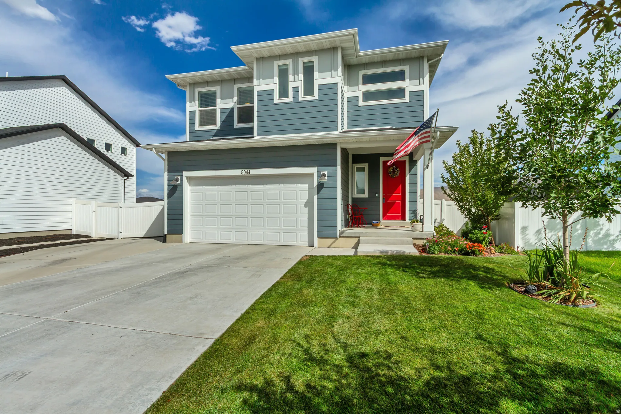 Modern exterior with multi-toned siding, attached two-car garage, concrete driveway, and a red entry door