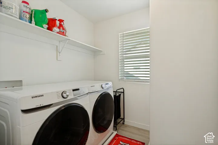 Laundry area featuring light wood-finish flooring, a white shelving unit, and a window with horizontal blinds