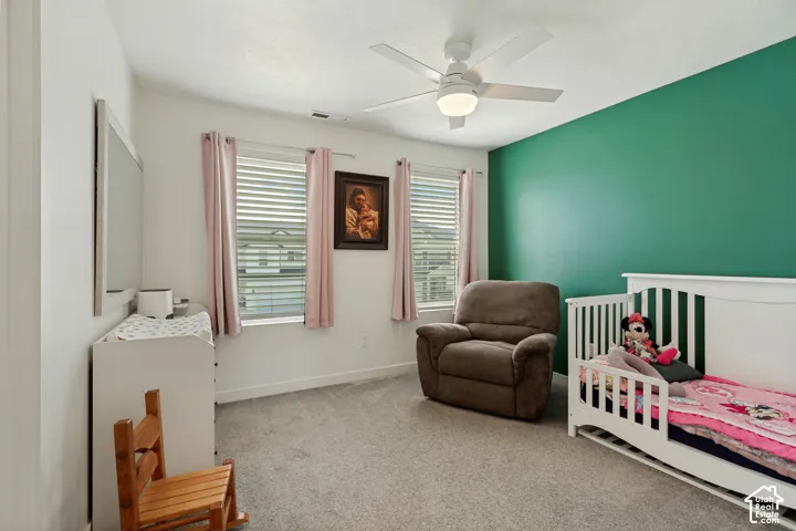 Carpeted interior space with a ceiling fan, dual windows, and an accent wall