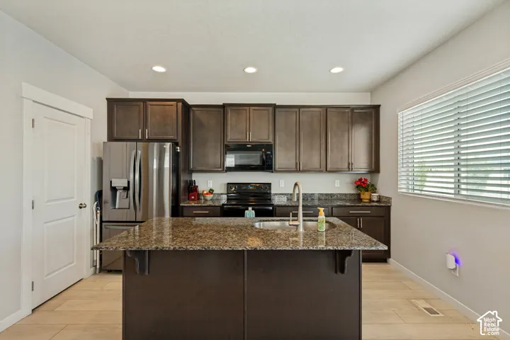 Kitchen featuring a large island with sink, dark wood cabinetry, stainless steel refrigerator, black range, and recessed lighting