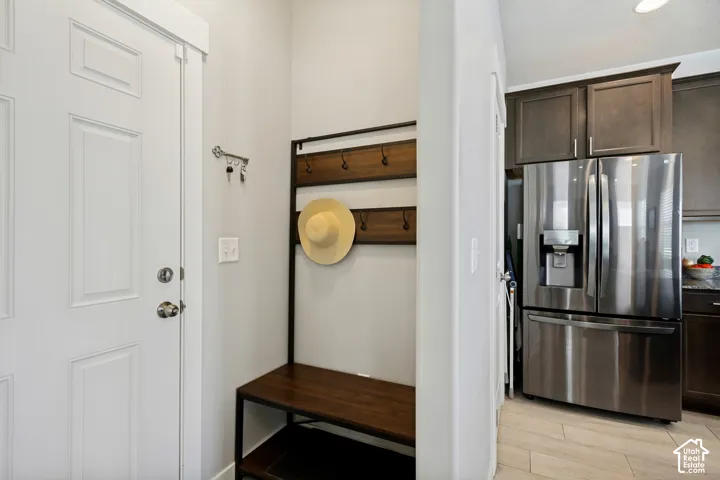 White paneled entry door, built-in coat rack with bench, stainless steel French door refrigerator, dark wood-finish cabinetry, and light wood-finish flooring