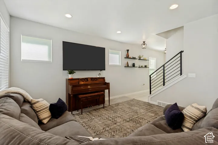Recessed ceiling lighting, multiple windows with blinds, built-in shelving, and a modern stair railing