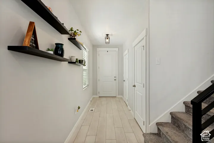 Light wood-finish flooring extending through the hallway, white doors with modern hardware, and a staircase with a black metal railing