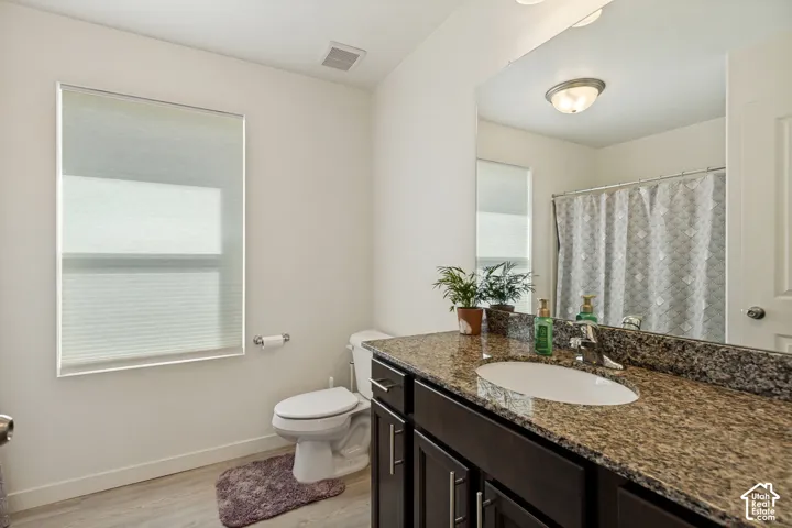 Bathroom featuring a single vanity with stone countertop, undermount sink, dark wood-finish cabinetry, and a full-width mirror