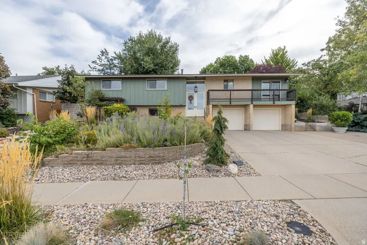 Split-level residence featuring a two-car garage, upper-level balcony, and mature landscaping