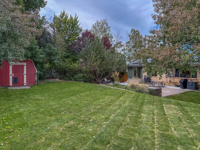 Expansive lawn, mature trees, red storage shed, paver patio, and stone retaining wall