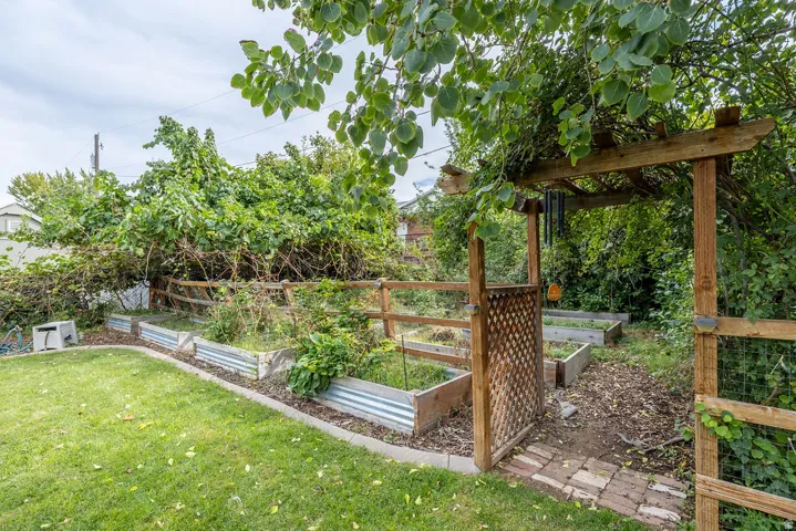 Expansive lawn area with a decorative wood arbor entryway, brick paver path, and multiple raised garden beds with corrugated metal accents