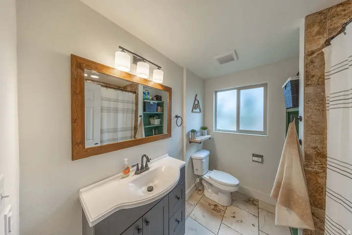 Vanity with integrated sink, wood-framed mirror, three-light fixture, frosted window, and tiled flooring