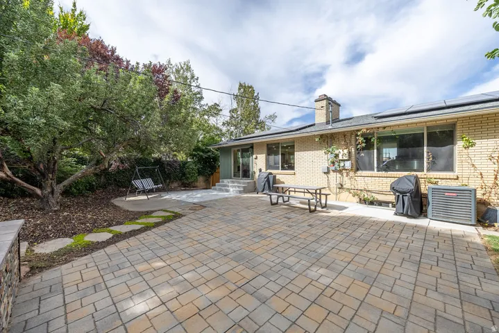 Brick exterior, solar panels, paver patio, mature landscaping, and an external air conditioning unit