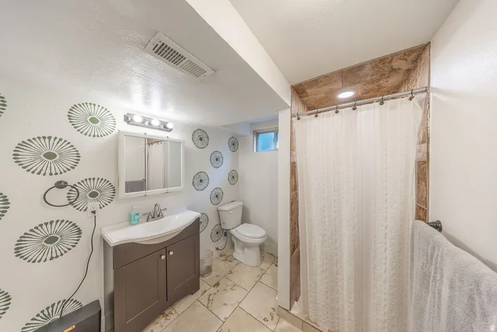 Bathroom featuring a single vanity with storage, a tiled shower surround, recessed lighting, and a window