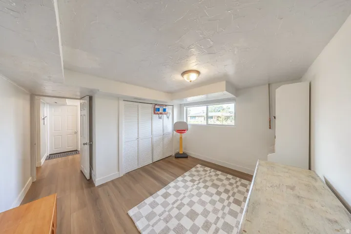 Wood-finish flooring, white louvered bifold closet doors, built-in storage cabinet, and a window for natural light