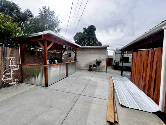 Concrete patio area featuring a covered outdoor structure with a metal roof and corrugated metal siding
