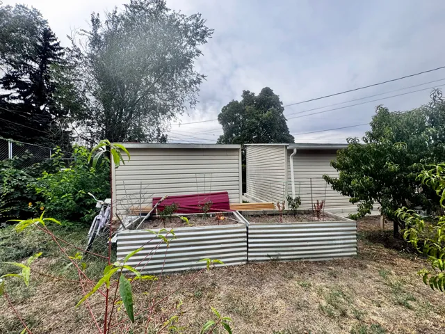 Exterior featuring vinyl siding, an attached gutter system, and two corrugated metal raised garden beds