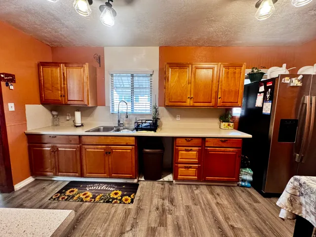 Kitchen featuring wood-finish flooring, wood cabinetry, light-colored countertops, and a double basin stainless steel sink with a high-arch faucet