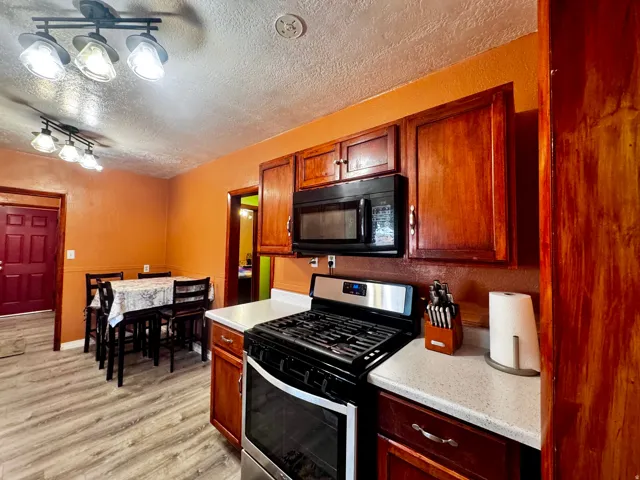 Wood-finish flooring, wood cabinetry, built-in microwave, gas range, and white countertops