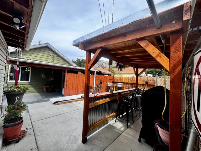 Concrete patio area featuring a built-in outdoor bar with a corrugated metal facade and a wood-frame overhead structure