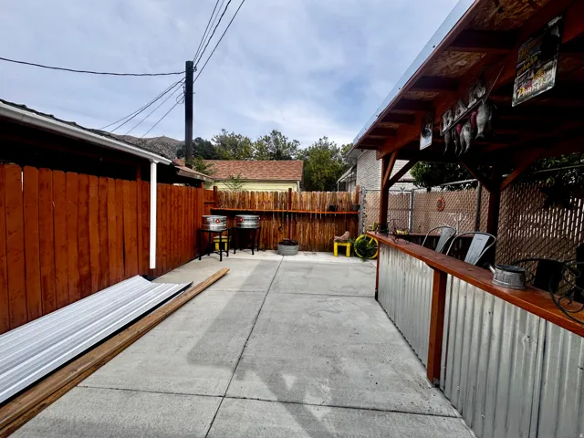 Concrete patio with a wood-framed overhead structure, featuring a corrugated metal and wood-top bar, and a privacy fence