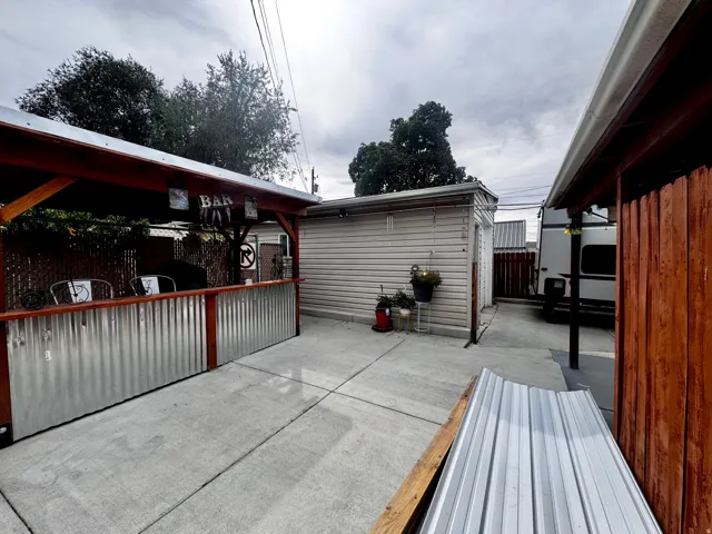 Outdoor entertaining area with a wood-framed structure, corrugated metal bar front, and concrete paving