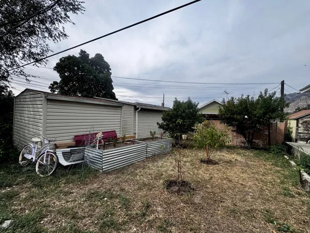 Backyard featuring two storage sheds, metal raised garden beds, and mature trees