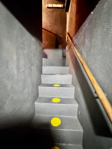 Staircase with a wood handrail, gray painted walls, and yellow circular accents on each step