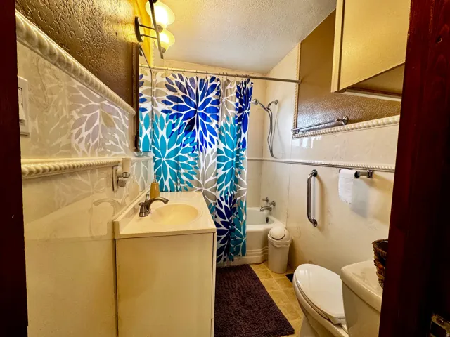 Bathroom featuring a vanity with integrated sink, wall-mounted cabinetry, a bathtub with shower, and tile wainscoting