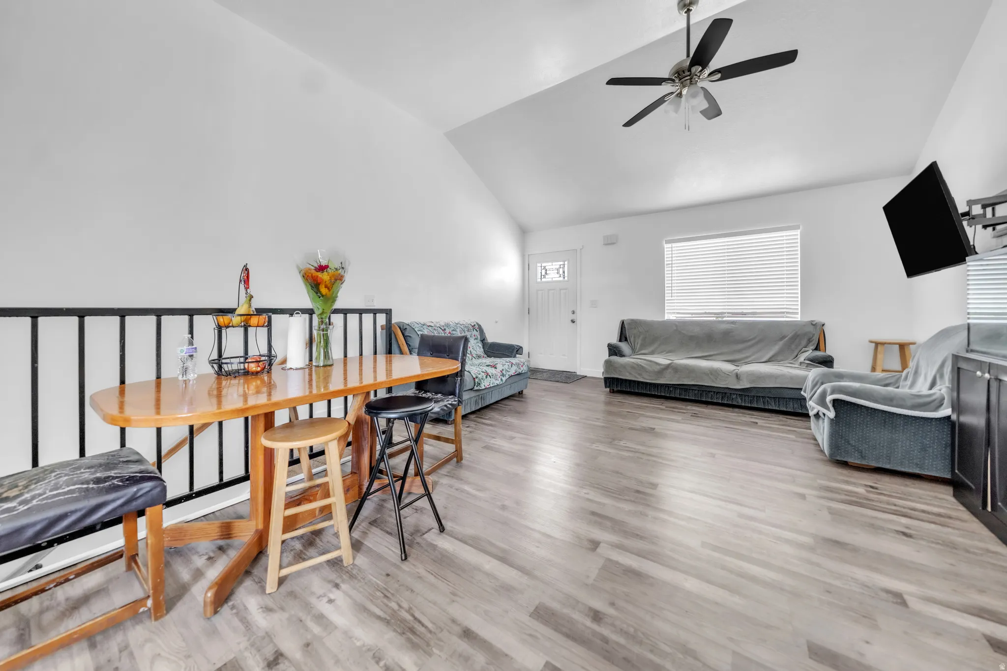 Vaulted ceiling, wood-finish flooring, ceiling fan, white paneled entry door, and a built-in media cabinet