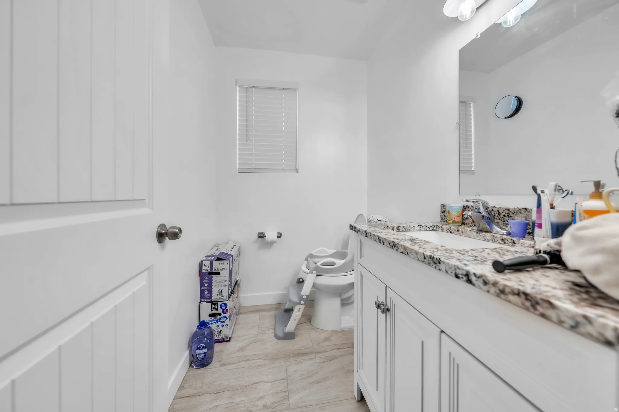 Bathroom featuring a white vanity with paneling, a stone countertop, an undermount sink, and a large wall-mounted mirror