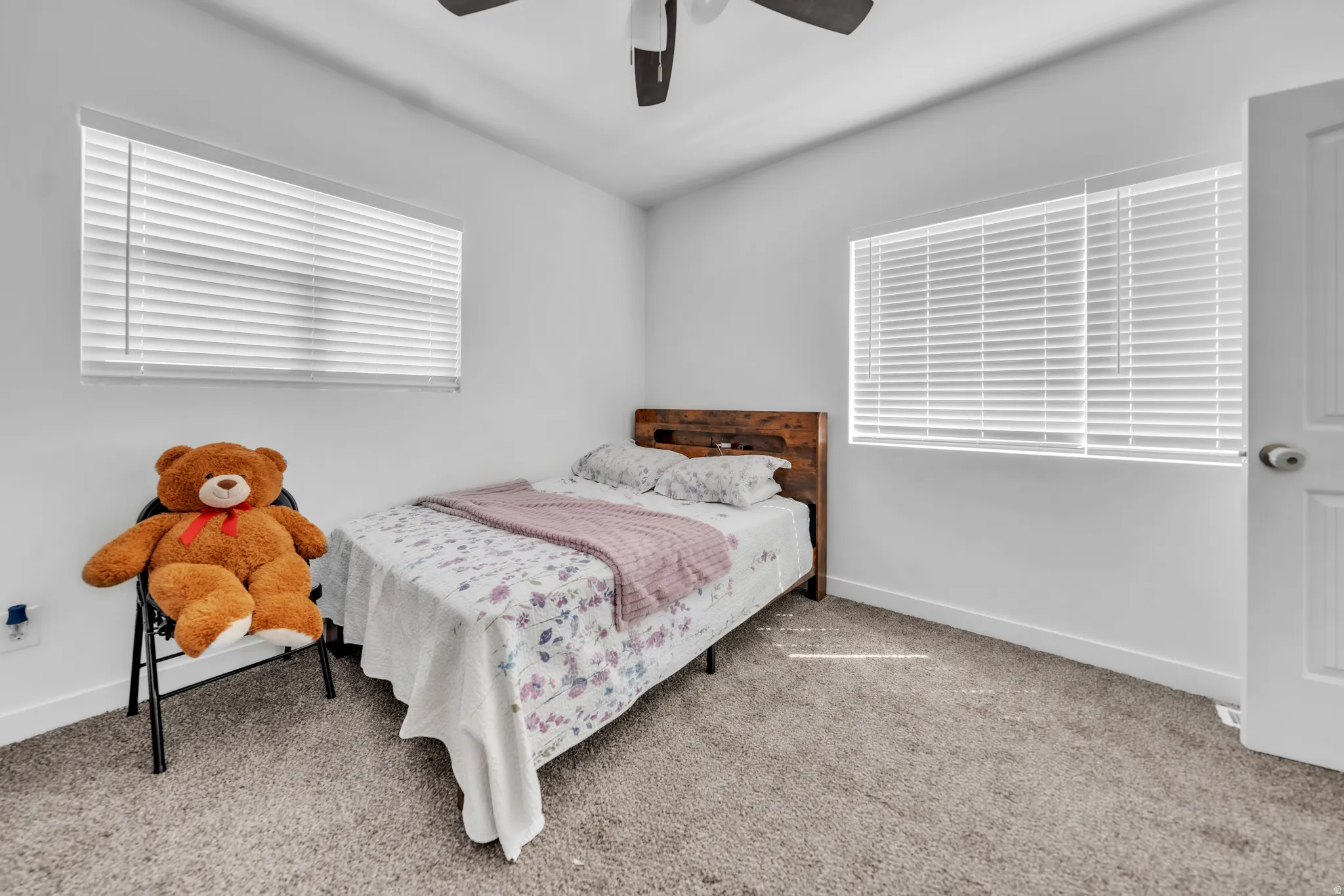 Plush carpeting, two windows with horizontal blinds, a ceiling fan, and a paneled interior door