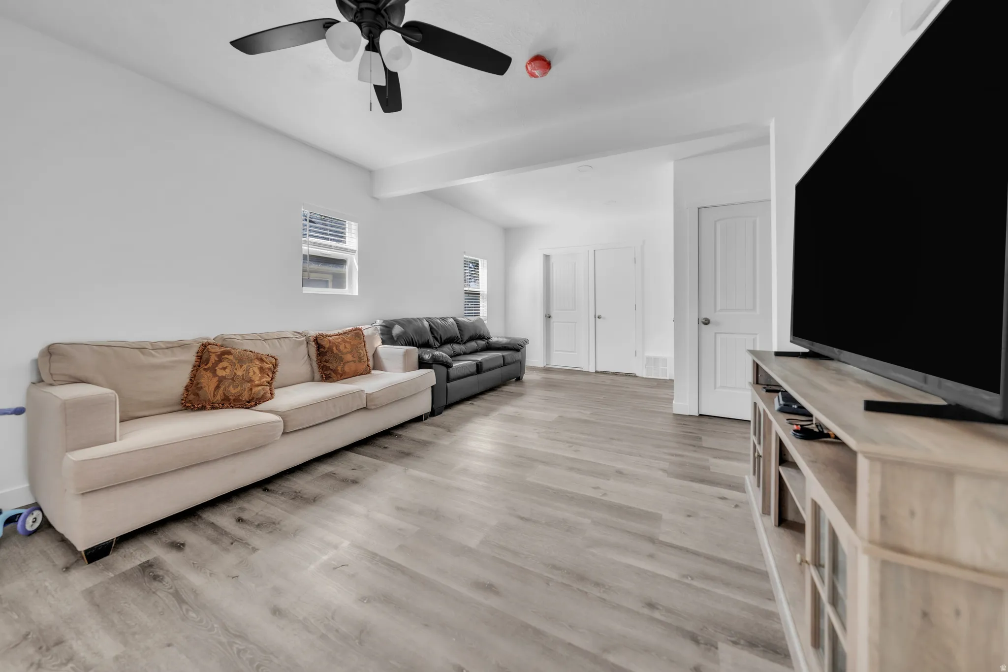 Light wood-finish flooring, white walls, and a ceiling fan with integrated lighting
