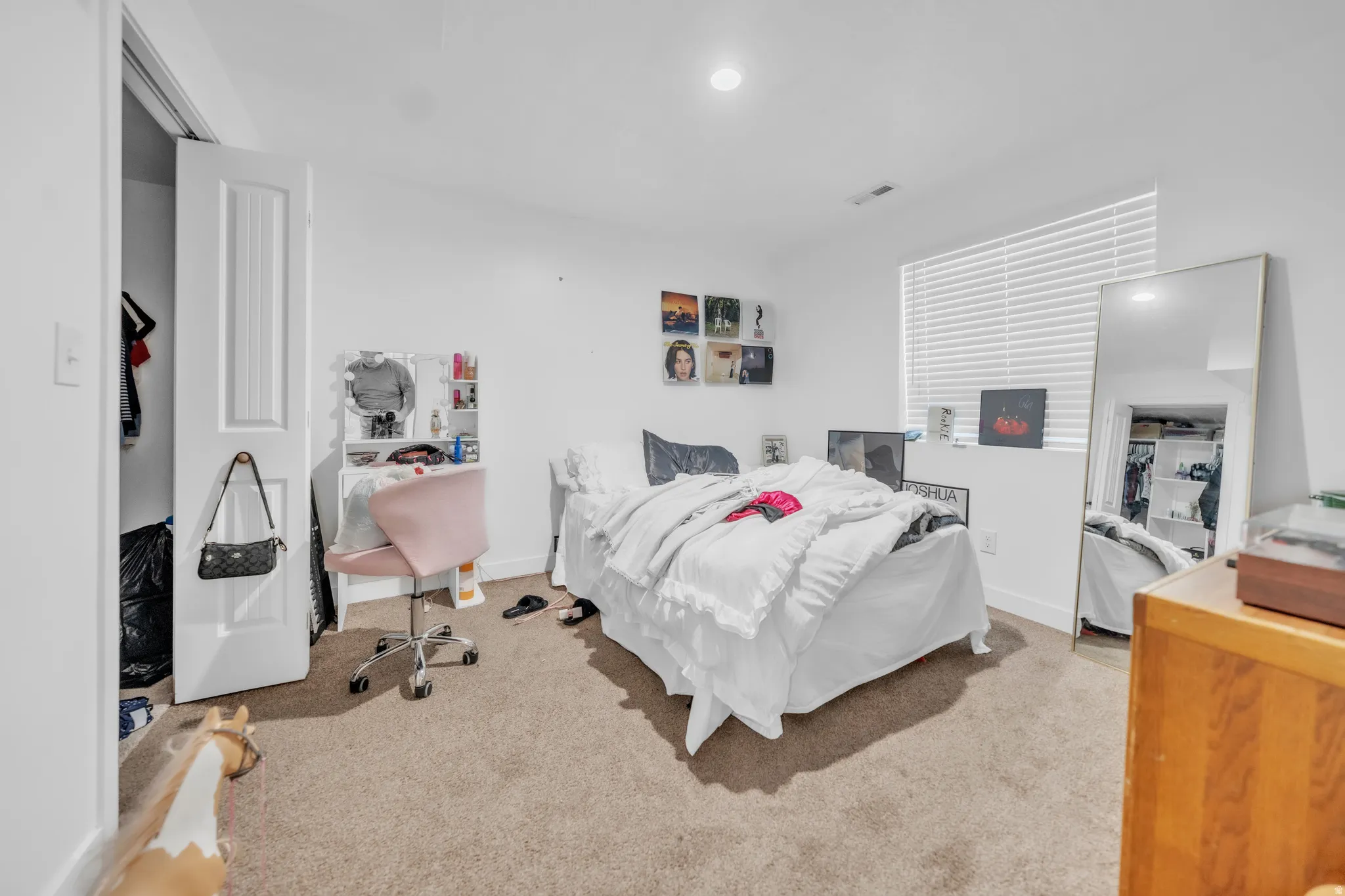 Recessed lighting illuminates the room, featuring a carpeted floor and a window with horizontal blinds