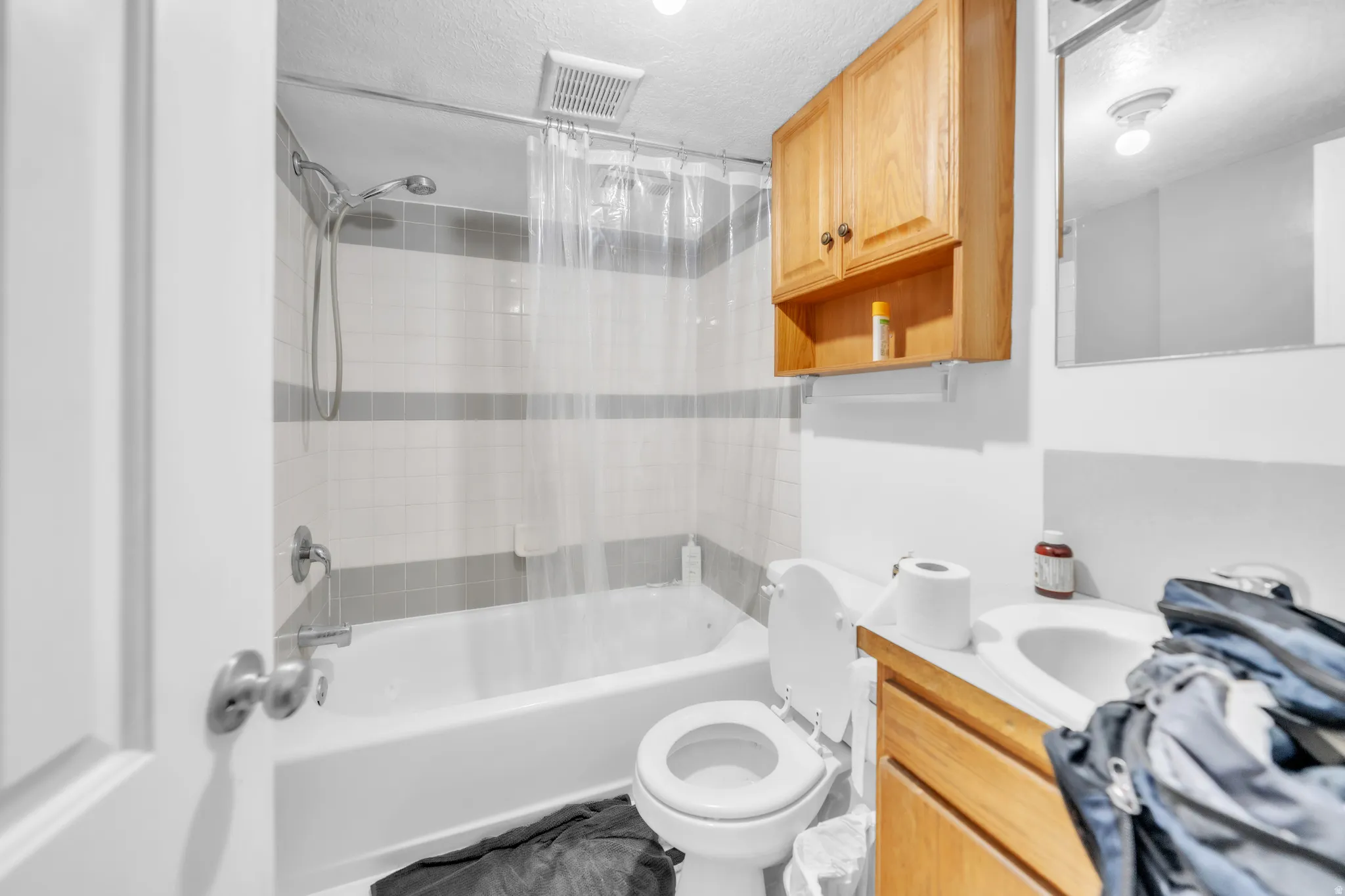 White subway tile shower surround with gray accent bands, built-in bathtub, chrome shower fixture, wood-finish vanity with integrated sink, and wall-mounted wooden cabinet