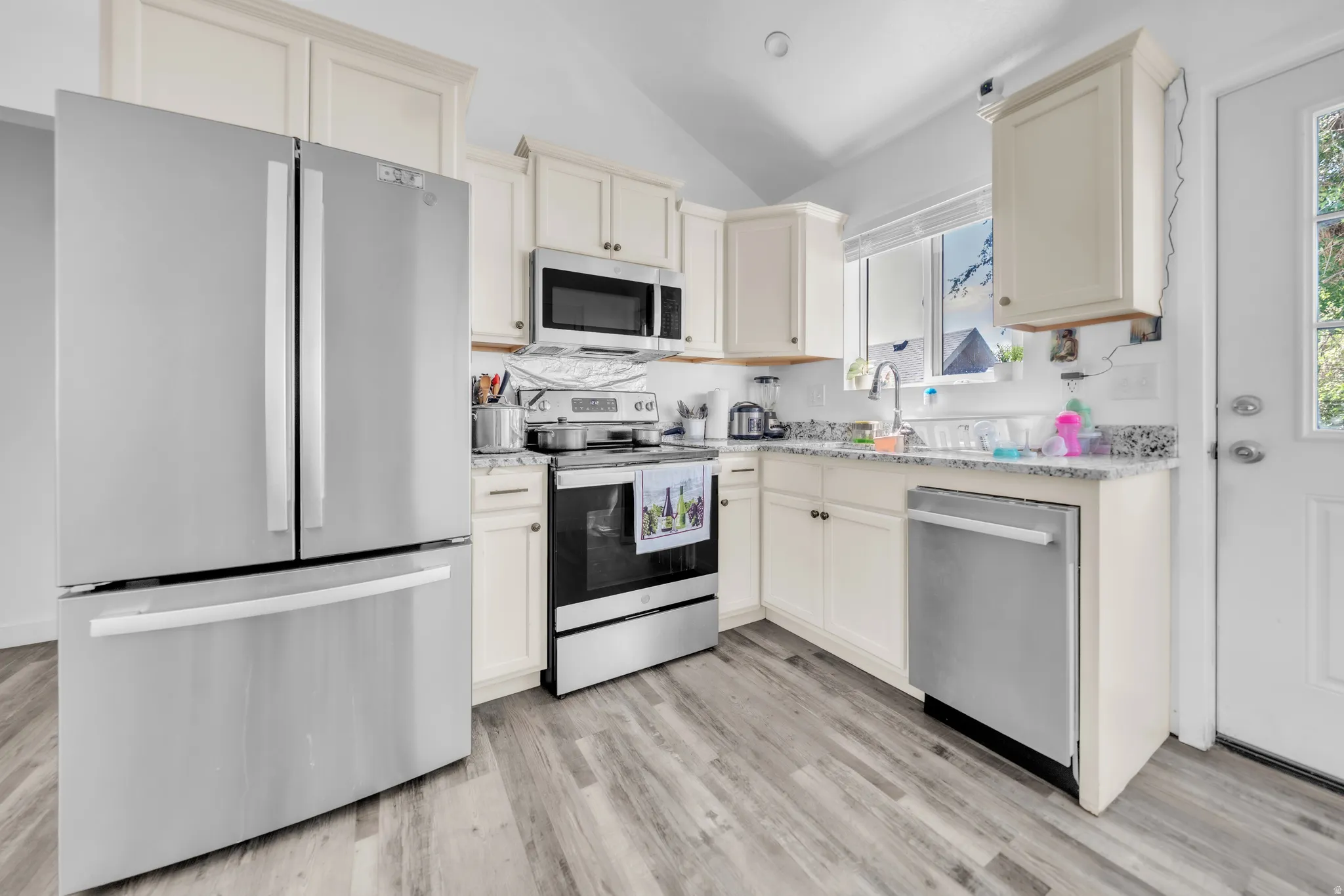 Kitchen featuring wood-finish flooring, vaulted ceiling, white cabinetry, speckled countertops, and stainless steel appliances