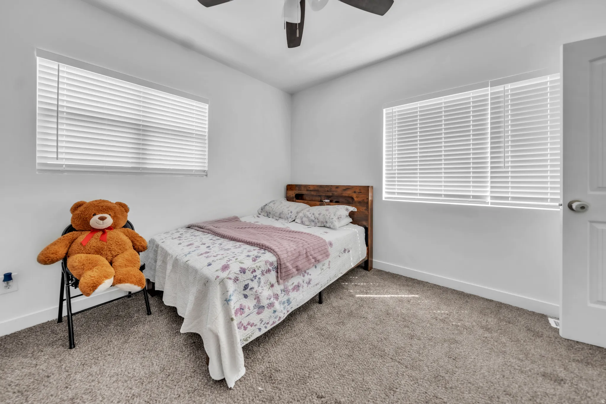 White walls, two windows with horizontal blinds, ceiling fan, carpeted flooring, and a white interior door