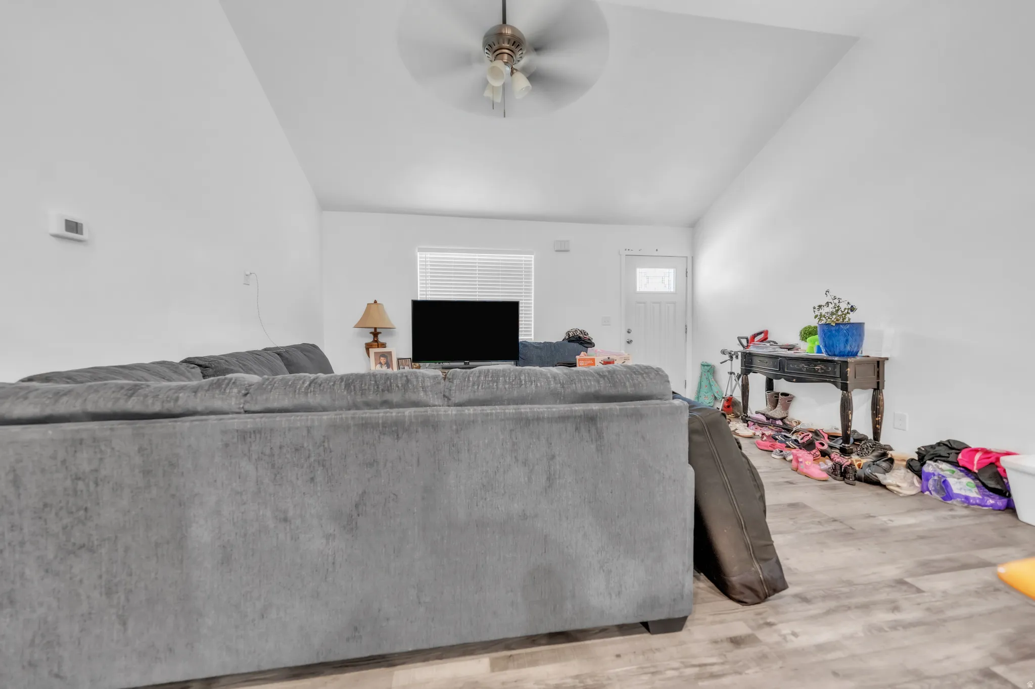 Vaulted ceiling, wood-finish flooring, ceiling fan, white interior walls, white paneled door with window insert