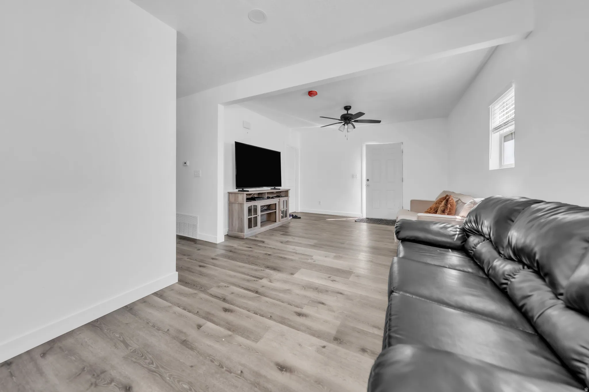 Wood-finish flooring throughout, white walls, and a ceiling fan with integrated lighting
