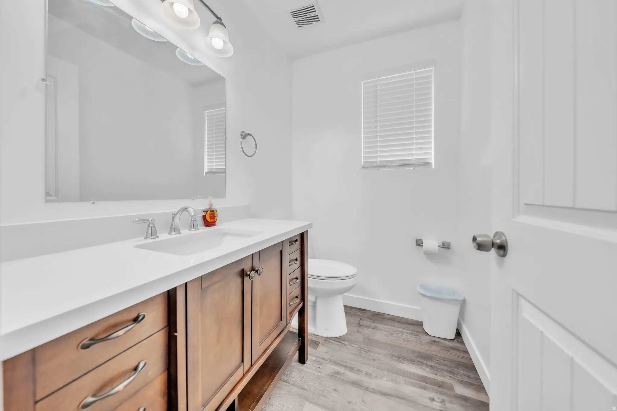 Wood-finish flooring with a white vanity featuring a built-in rectangular sink, a white countertop, and a large wall mirror
