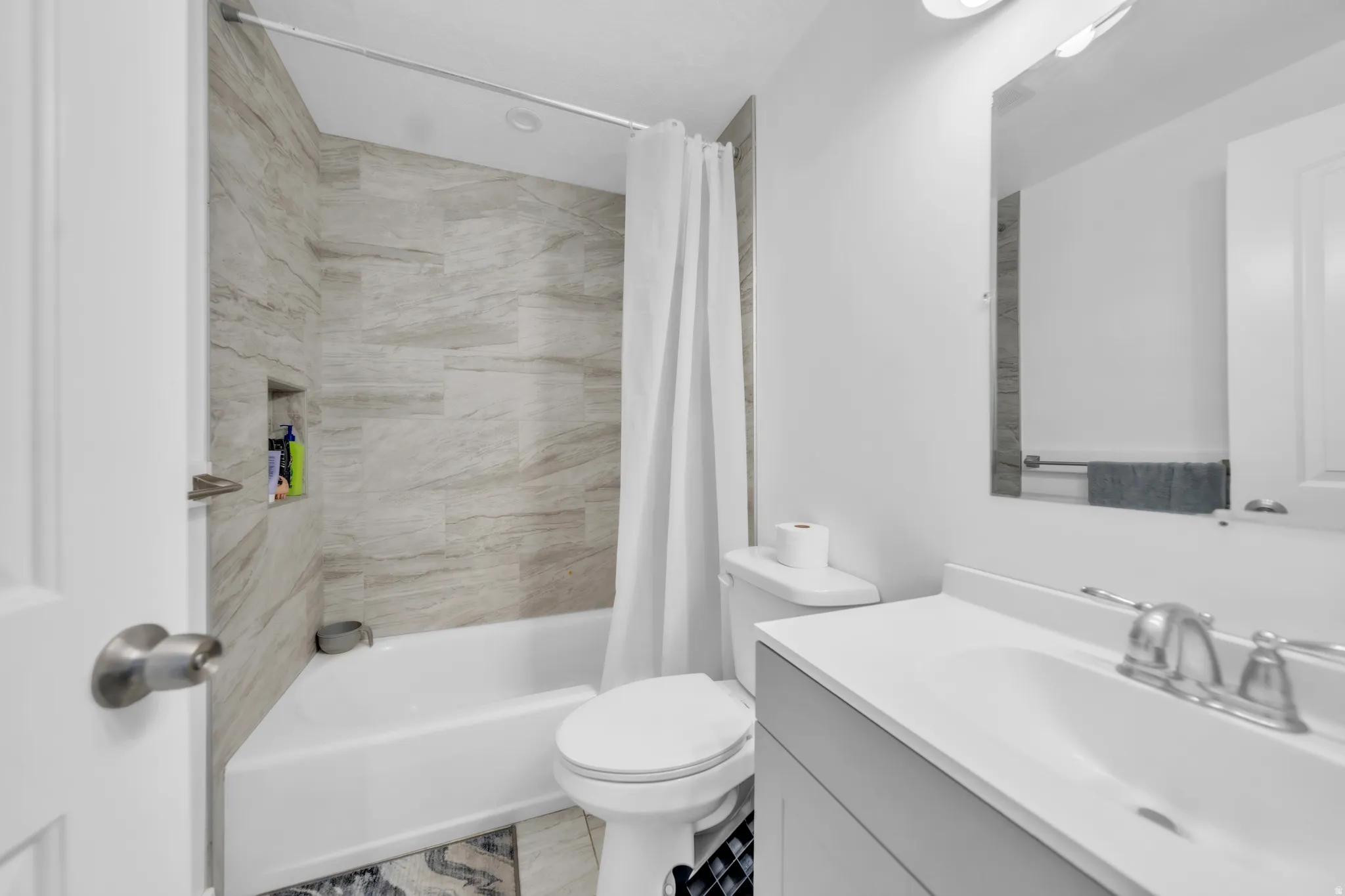 Bathtub with tiled surround and built-in niche, single vanity with integrated sink, and wall-mounted mirror