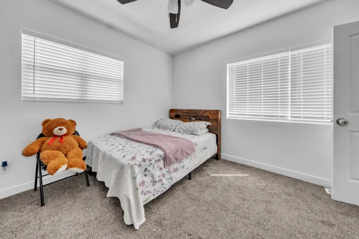 White walls, two windows with horizontal blinds, ceiling fan, carpeted flooring, and a white interior door