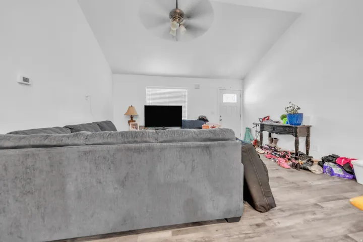 Vaulted ceiling, wood-finish flooring, ceiling fan, white interior walls, white paneled door with window insert