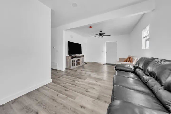 Wood-finish flooring throughout, white walls, and a ceiling fan with integrated lighting
